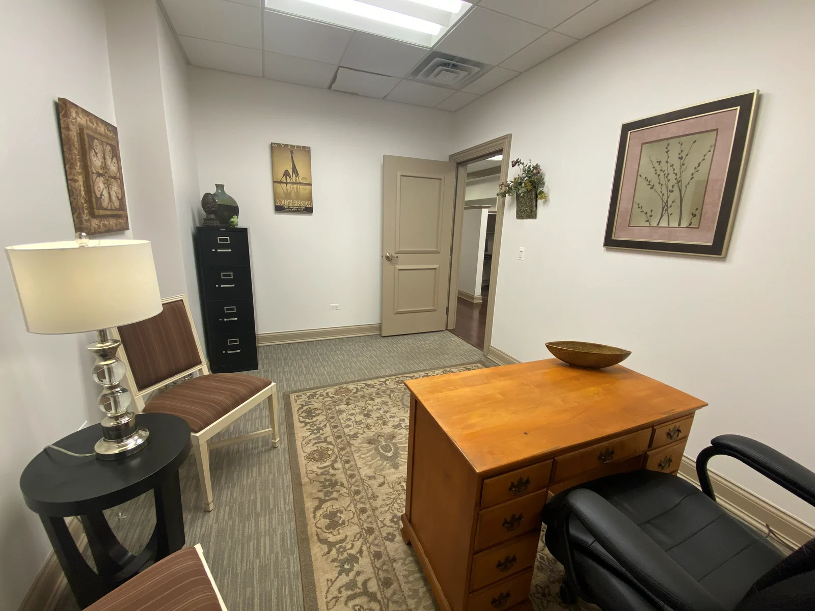 Suite 102C furnished office looking toward the door, with guest chair, lamp, and filing cabinet - St. Charles, IL
